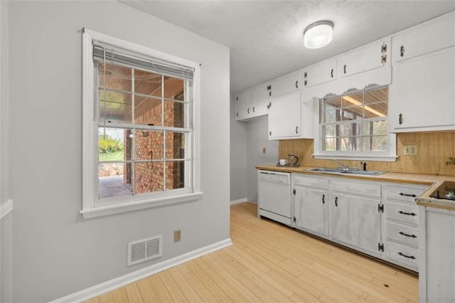 kitchen with visible vents, light wood-style flooring, white dishwasher, white cabinets, and a sink