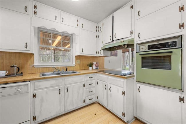 kitchen with under cabinet range hood, white appliances, white cabinets, and a sink