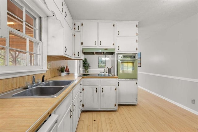 kitchen featuring a healthy amount of sunlight, a sink, oven, white cabinetry, and black electric cooktop