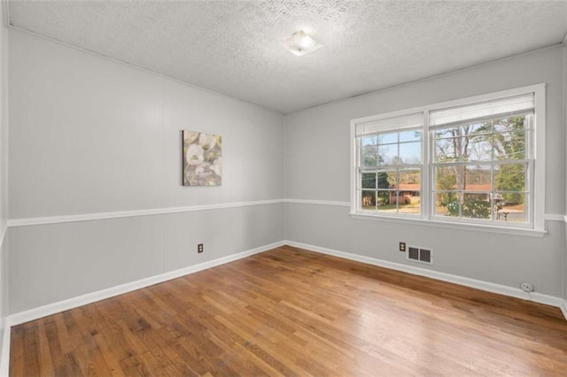 spare room featuring visible vents, a textured ceiling, baseboards, and wood finished floors