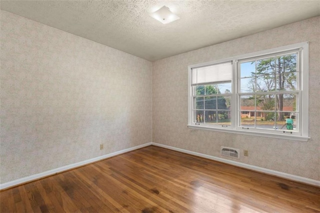 spare room featuring visible vents, a textured ceiling, baseboards, and wood finished floors