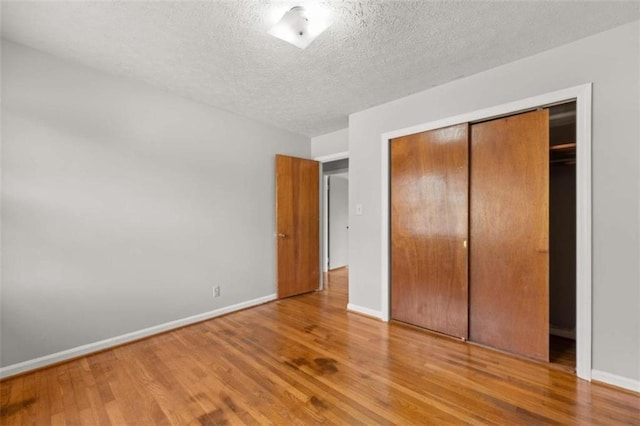 unfurnished bedroom with a closet, a textured ceiling, baseboards, and wood finished floors