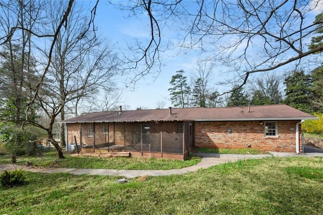 back of house featuring brick siding, a lawn, and a sunroom