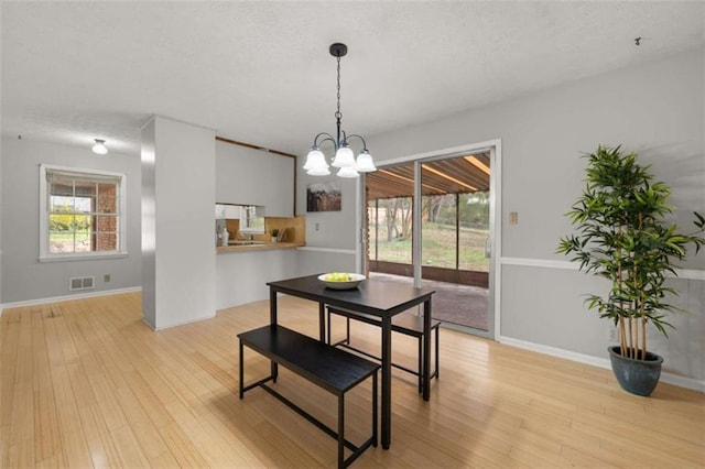 dining room with light wood finished floors, visible vents, a healthy amount of sunlight, and an inviting chandelier