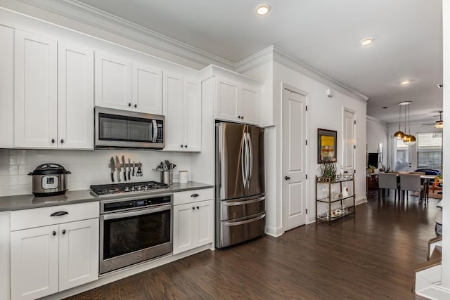 kitchen with dark countertops, dark wood-style floors, appliances with stainless steel finishes, crown molding, and white cabinetry