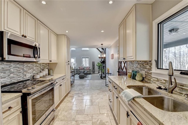 kitchen with stainless steel appliances, stone tile flooring, a sink, and cream cabinets