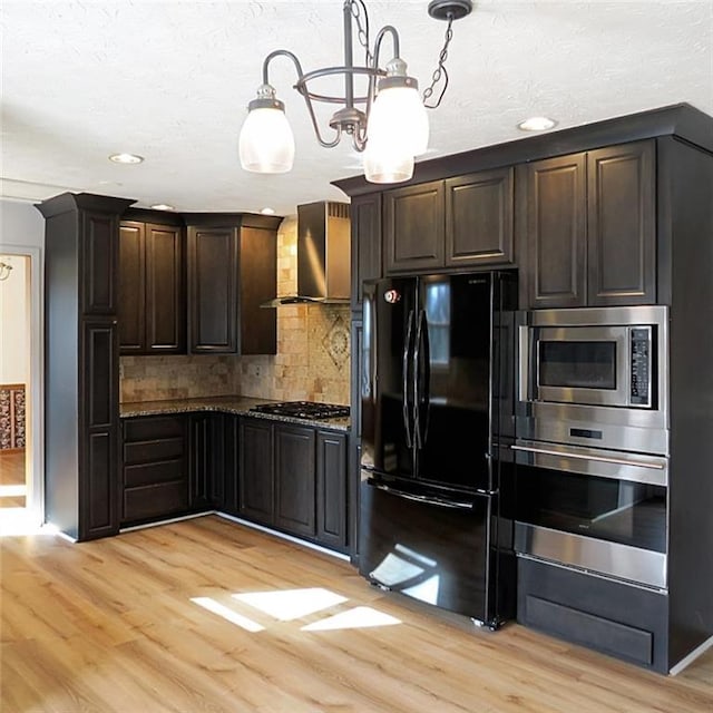 kitchen with dark brown cabinetry, wall chimney range hood, light wood-style flooring, and stainless steel appliances