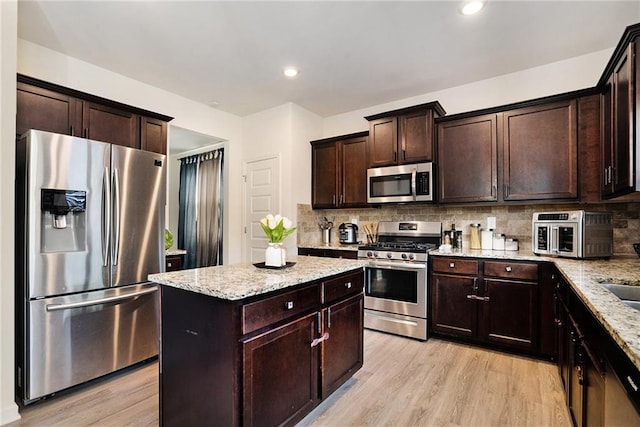 kitchen with light hardwood / wood-style floors, light stone countertops, stainless steel appliances, and tasteful backsplash