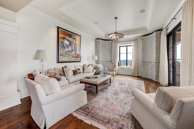 living room featuring a notable chandelier, dark wood-type flooring, ornamental molding, and a tray ceiling