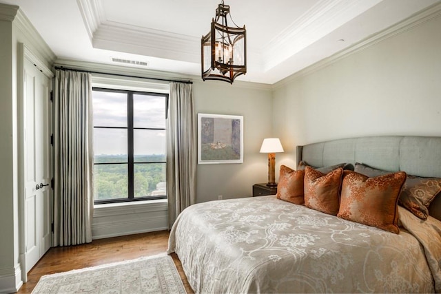 bedroom featuring a chandelier, hardwood / wood-style floors, a tray ceiling, and crown molding