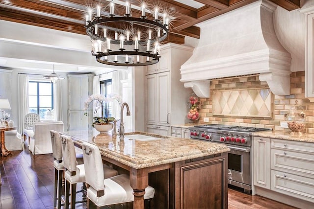 kitchen with a center island with sink, custom range hood, decorative backsplash, designer stove, and sink