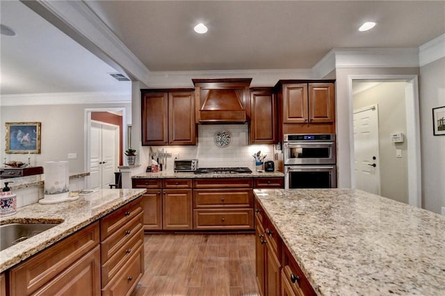 kitchen with visible vents, appliances with stainless steel finishes, custom exhaust hood, light wood-style floors, and backsplash