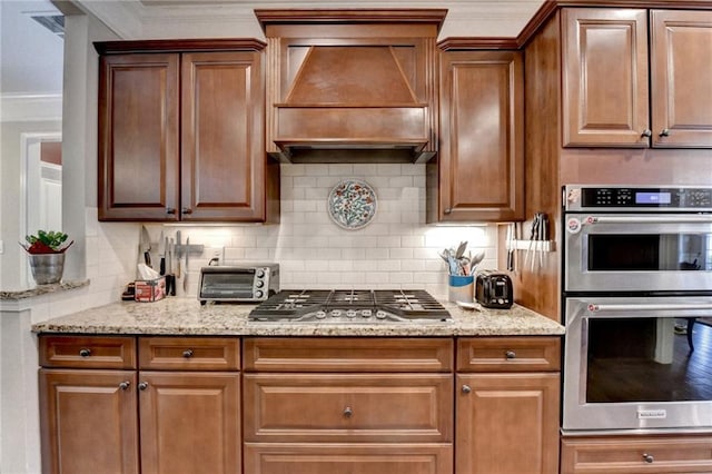 kitchen featuring a toaster, custom range hood, backsplash, appliances with stainless steel finishes, and ornamental molding