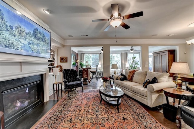 living area with ornamental molding, a glass covered fireplace, dark wood finished floors, and visible vents