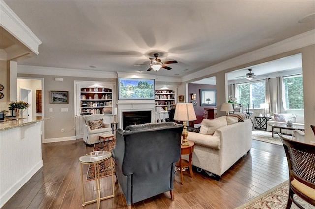 living room featuring dark wood-style flooring, a fireplace, built in features, baseboards, and ornamental molding