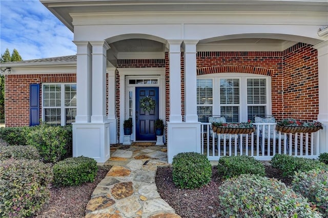 entrance to property featuring a porch and brick siding