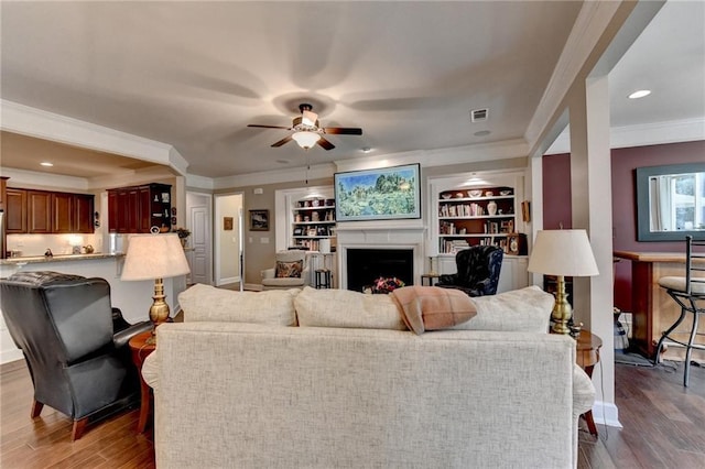 living area with crown molding, a fireplace, visible vents, and wood finished floors