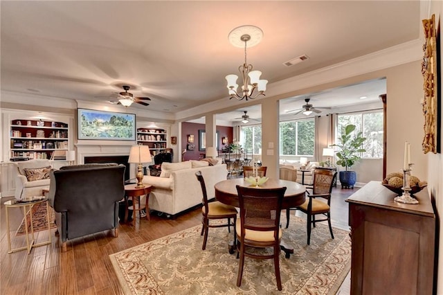 dining space featuring built in features, visible vents, wood finished floors, crown molding, and a fireplace