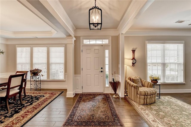 foyer entrance with ornamental molding, dark wood-style flooring, visible vents, and a chandelier