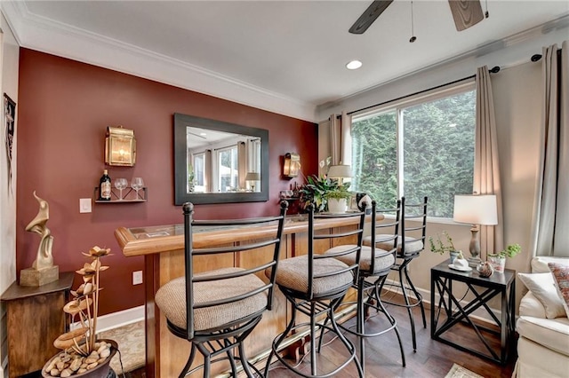 bar featuring baseboards, a ceiling fan, wood finished floors, crown molding, and a bar