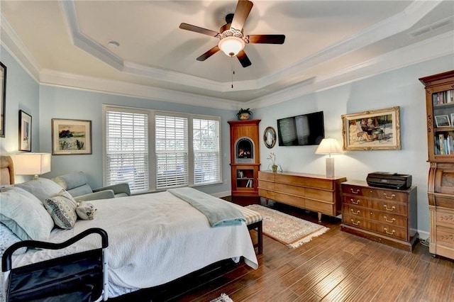 bedroom featuring a tray ceiling, wood finished floors, visible vents, and crown molding