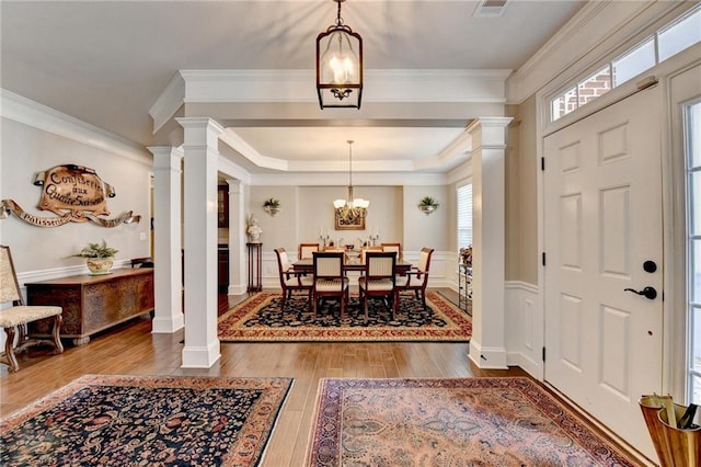 entryway featuring ornate columns, ornamental molding, wood finished floors, and an inviting chandelier