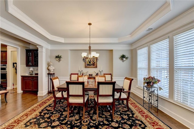 dining area with dark wood-style floors, a tray ceiling, ornamental molding, and an inviting chandelier