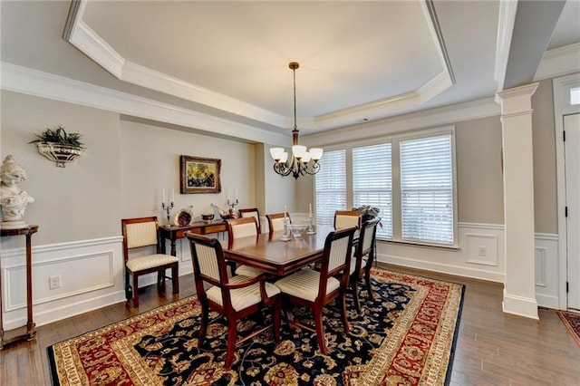 dining area featuring dark wood-style floors, a raised ceiling, a wainscoted wall, and decorative columns