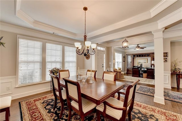 dining space with a decorative wall, wood finished floors, wainscoting, a tray ceiling, and decorative columns