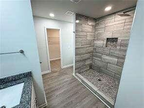 bathroom with tiled shower and wood-type flooring