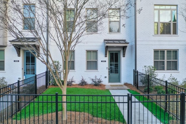 view of front facade with a fenced front yard, brick siding, a front yard, and a gate