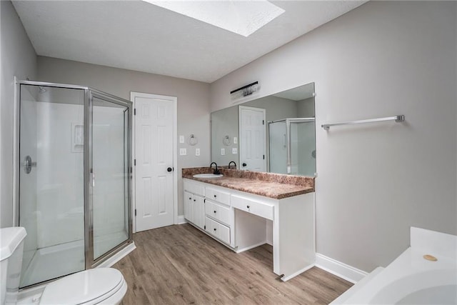 bathroom featuring a skylight, toilet, wood finished floors, vanity, and a shower stall