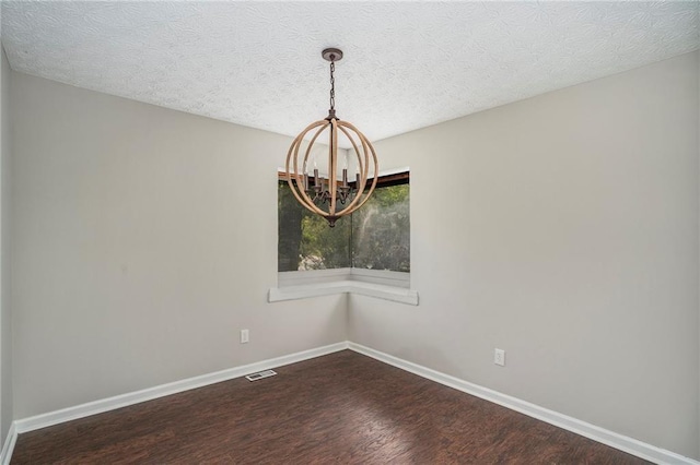 spare room featuring a chandelier, a textured ceiling, visible vents, baseboards, and dark wood finished floors