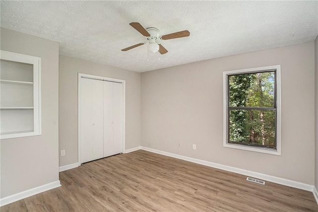 unfurnished bedroom featuring baseboards, a textured ceiling, visible vents, and wood finished floors