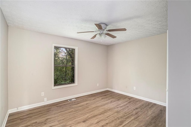 empty room featuring visible vents, a ceiling fan, a textured ceiling, wood finished floors, and baseboards