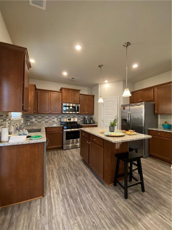 kitchen with dark wood-style floors, backsplash, appliances with stainless steel finishes, and a kitchen island