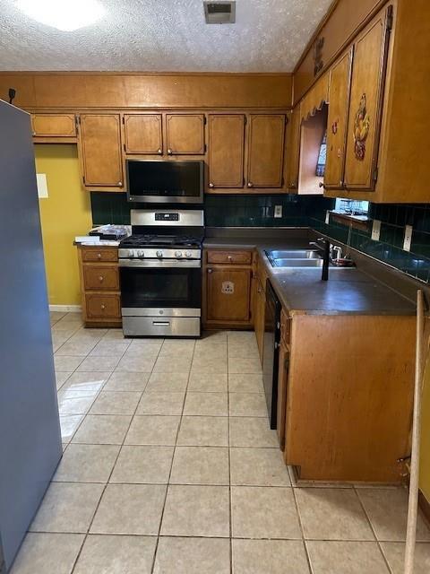 kitchen featuring sink, backsplash, light tile patterned floors, stainless steel appliances, and a textured ceiling