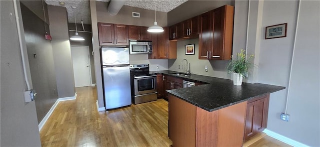 kitchen with appliances with stainless steel finishes, a sink, light wood finished floors, and a peninsula