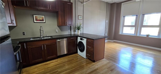 kitchen with washer / dryer, a sink, appliances with stainless steel finishes, light wood-type flooring, and a peninsula