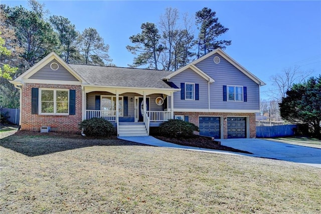 tri-level home featuring a porch, a garage, brick siding, fence, and driveway