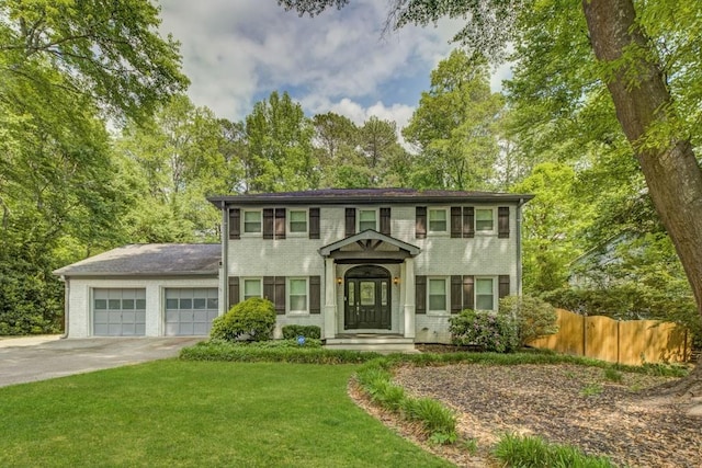 colonial home featuring fence, an attached garage, a front lawn, brick siding, and driveway