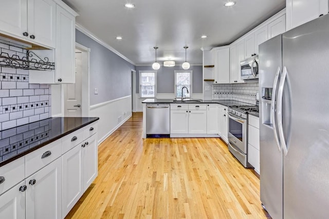 kitchen featuring white cabinets, dark countertops, a sink, stainless steel appliances, and a peninsula