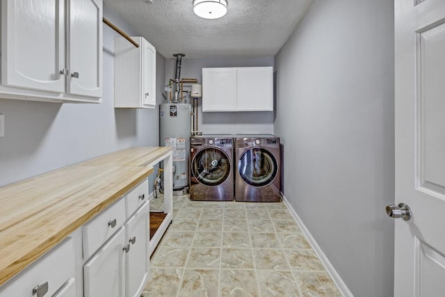 laundry area with gas water heater, a textured ceiling, washing machine and dryer, cabinet space, and baseboards