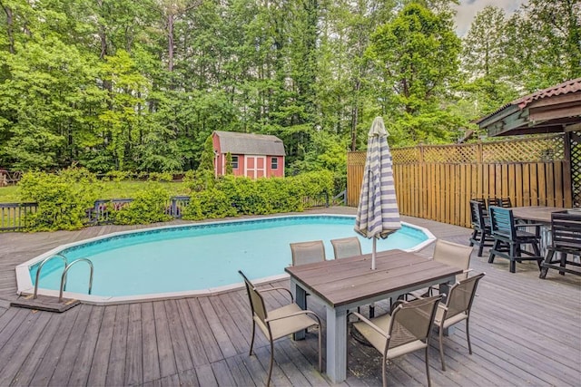 view of pool with a deck, a fenced in pool, outdoor dining area, and a shed