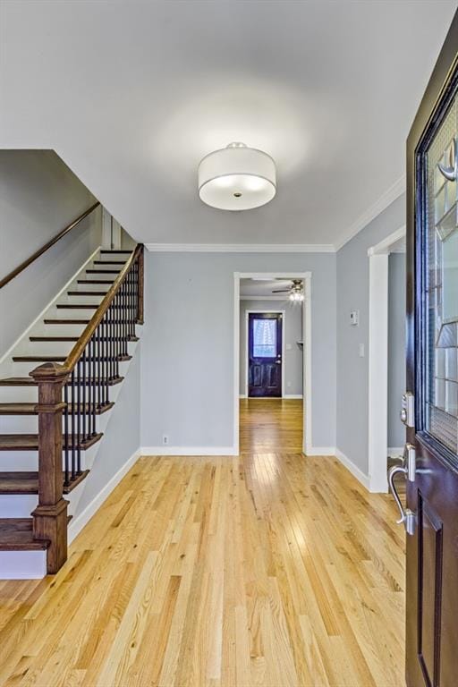 foyer entrance with ceiling fan, crown molding, wood finished floors, baseboards, and stairs
