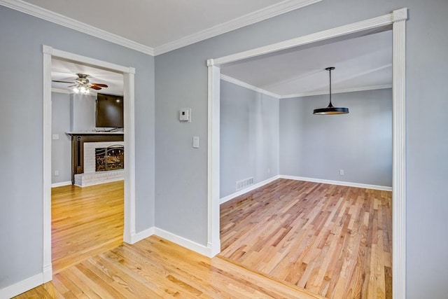 empty room with ceiling fan, a fireplace, baseboards, wood finished floors, and visible vents
