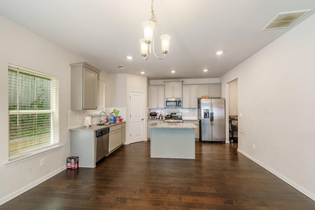 kitchen with sink, appliances with stainless steel finishes, decorative light fixtures, a kitchen island, and dark hardwood / wood-style flooring