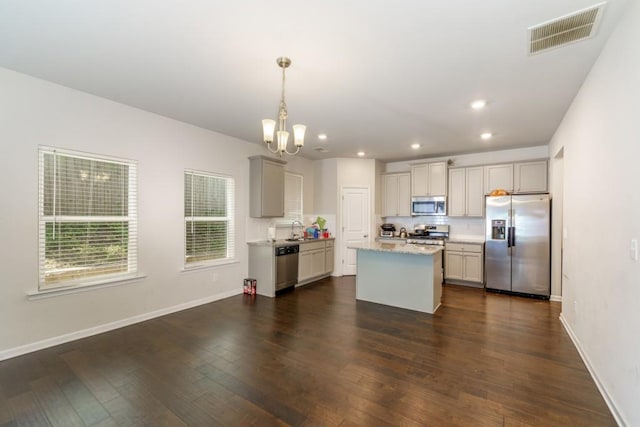 kitchen with appliances with stainless steel finishes, dark hardwood / wood-style flooring, a kitchen island, and hanging light fixtures