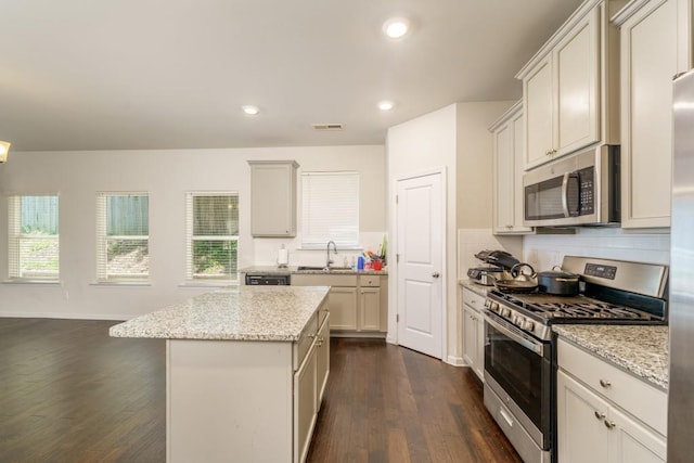 kitchen with appliances with stainless steel finishes, light stone counters, dark wood-type flooring, white cabinets, and a kitchen island