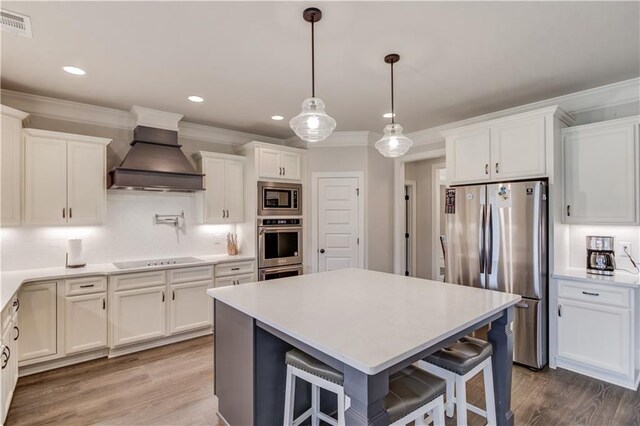 kitchen with white cabinets, hardwood / wood-style flooring, a breakfast bar area, appliances with stainless steel finishes, and premium range hood